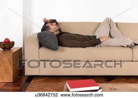 "Side view of mature man lying on back on sofa hand on forehead, looking up" View Large Photo Image Stock Image - "Side view of mature man lying on back on sofa hand on forehead, looking up". Fotosearch
