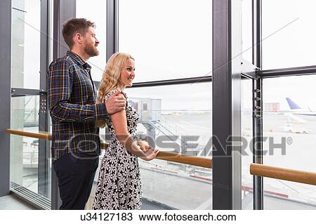 Side view of mid adult couple standing looking out of airport window View Large Photo Image Stock Image - Side view of mid adult couple standing looking out of airport window. Fotosearch