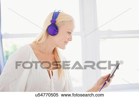 Side view of young woman looking at smartphone wearing headphones smiling View Large Photo Image Stock Photography - Side view of young woman looking at smartphone wearing headphones smiling. Fotosearch