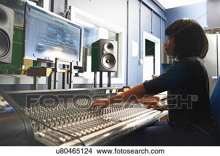 "Side view of young woman sitting at mixing desk in recording studio looking at monitor, adjusting controls" View Large Photo Image Picture - "Side view of young woman sitting at mixing desk in recording studio looking at monitor, adjusting controls". Fotosearch