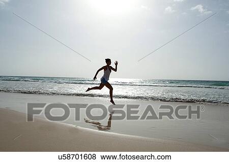 Stock Photo - "Silhouetted mid adult woman running barefoot on beach, Cape Verde, Africa". Fotosearch