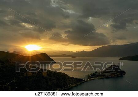 Stock Image - "Silhouetted mountains and Lugu Lake at sunrise, Yunnan, China". Fotosearch