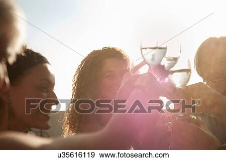 "Small group of friends making a toast smiling, lens flare" View Large Photo Image Stock Photo - "Small group of friends making a toast smiling, lens flare". Fotosearch