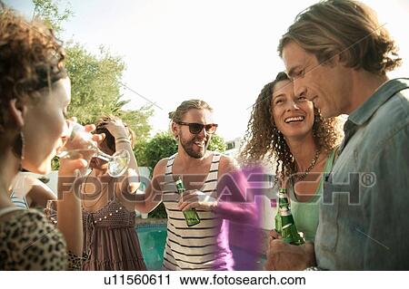 "Small group of friends standing holding drinks talking and smiling, lens flare" View Large Photo Image Stock Image - "Small group of friends standing holding drinks talking and smiling, lens flare". Fotosearch