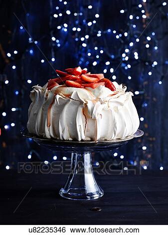 Stock Photograph - Strawberry covered pavlova on glass cake stand in front of sparkly navy blue background. Fotosearch