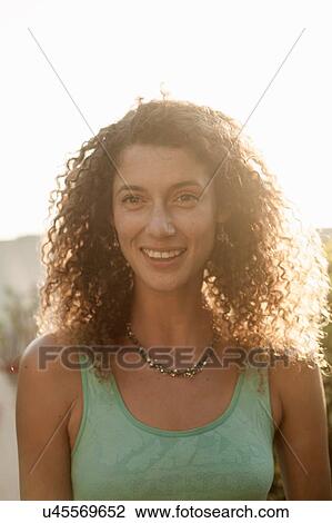 Stock Image - Sunlit portrait of young woman with curly hair. Fotosearch