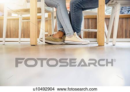 Picture - Surface level view of couples entwined legs sitting at table face to face. Fotosearch