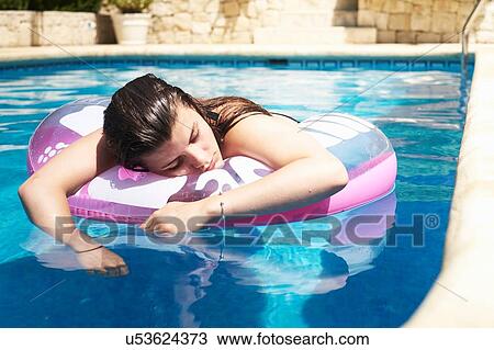 Stock Image - Teenage girl floating on inflatable in swimming pool. Fotosearch