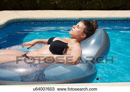 Stock Image - Teenage girl lying on inflatable in swimming pool. Fotosearch