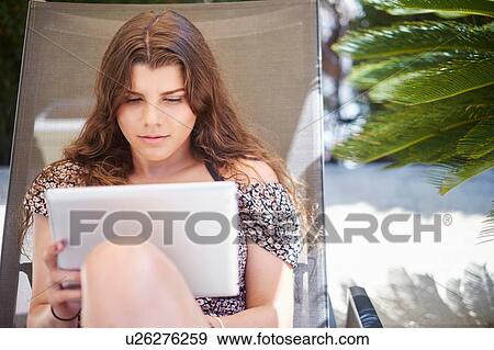 Teenage girl sitting on sun lounger using digital tablet View Large Photo Image Stock Photo - Teenage girl sitting on sun lounger using digital tablet. Fotosearch