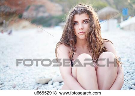 Stock Photo - "Teenage girl with long brown hair hugging knees on beach, Javea, Spain". Fotosearch