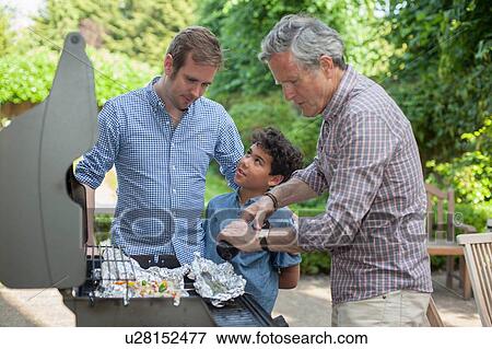 Stock Photo - Three generation family cooking on barbecue. Fotosearch