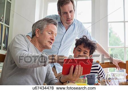 Stock Photo - Three generation family looking at digital tablet. Fotosearch
