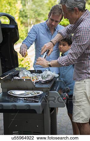 Stock Image - Three generation family preparing food on barbecue. Fotosearch