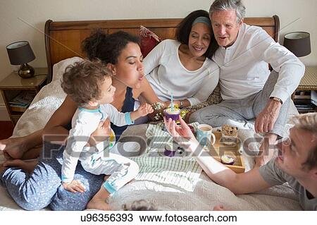 "Three generation family sitting on bed, blowing out candle on cupcake" View Large Photo Image Stock Image - "Three generation family sitting on bed, blowing out candle on cupcake". Fotosearch