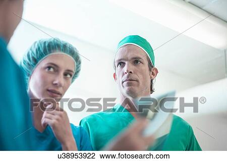 Stock Image - Three male and female surgeons having discussion in hospital. Fotosearch