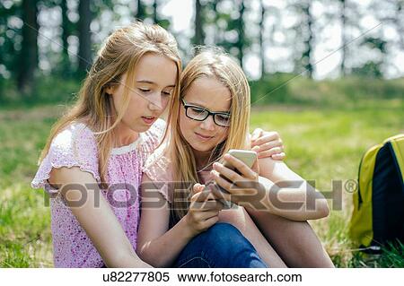 "Two young girls, outdoors, looking at smartphone" View Large Photo Image Stock Photography - "Two young girls, outdoors, looking at smartphone". Fotosearch