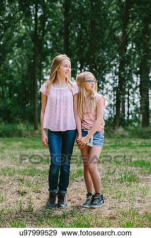 Stock Photo - "Two young girls standing together in field, looking away". Fotosearch