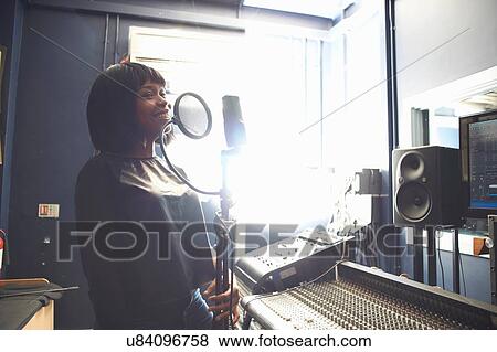 Stock Photo - Waist up of young woman in recording studio singing into microphgone through pop guard. Fotosearch