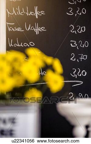 Stock Photograph - "Yellow flowers in front of cafes chalkboard menu, focus on background". Fotosearch