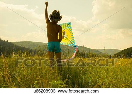 Stock Image - "Young boy flying kite in field, rear view". Fotosearch