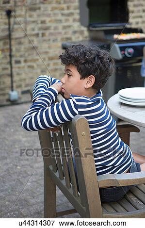 Young boy sitting on chair in garden View Large Photo Image Stock Photo - Young boy sitting on chair in garden. Fotosearch