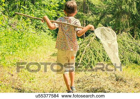 Picture - "Young boy walking through field, carrying fishing net, rear view". Fotosearch