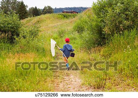 Stock Photograph - "Young boy walking through field, carrying fishing net, rear view". Fotosearch