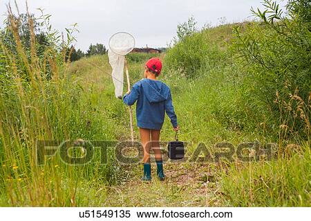 Stock Photography - "Young boy walking through field, carrying fishing net, rear view". Fotosearch