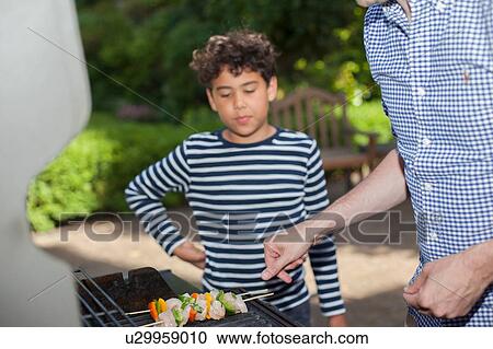 Young boy watching father cook on barbecue View Large Photo Image Stock Image - Young boy watching father cook on barbecue. Fotosearch