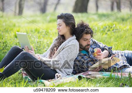Young couple back to back reading and using digital tablet in woodland View Large Photo Image Stock Photo - Young couple back to back reading and using digital tablet in woodland. Fotosearch
