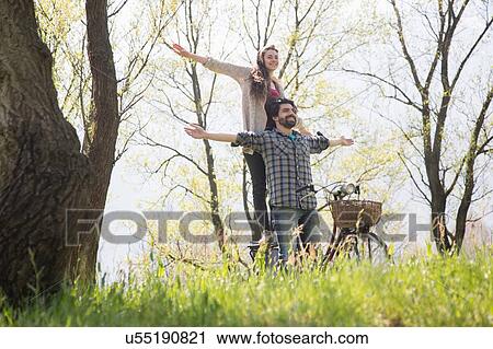 Stock Image - Young couple on bicycle with arms open in rural woodland. Fotosearch