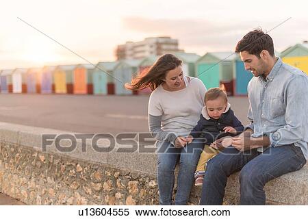 Stock Photography - Young family sitting on beach wall. Fotosearch