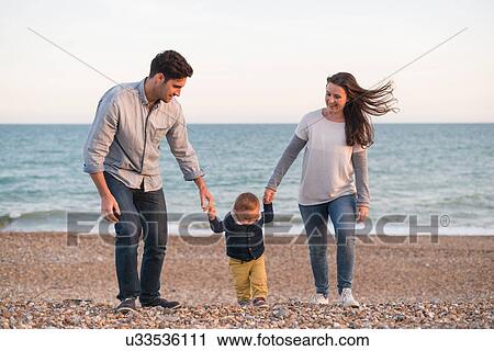 Young family walking along pebble beach hand in hand View Large Photo Image Stock Image - Young family walking along pebble beach hand in hand. Fotosearch