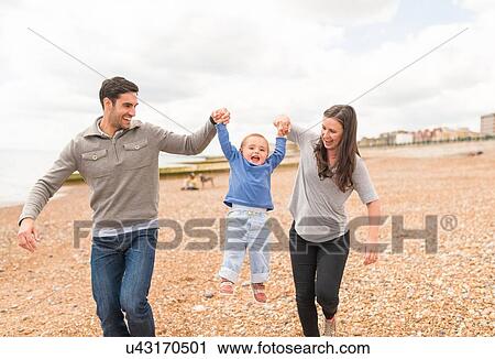 Young family walking hand in hand along pebble beach View Large Photo Image Stock Image - Young family walking hand in hand along pebble beach. Fotosearch