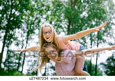 Picture - "Young girl, balancing on sister's back, outdoors, laughing". Fotosearch