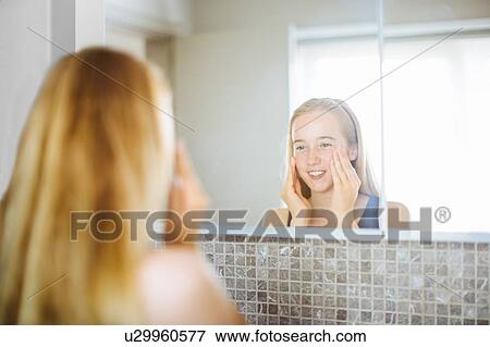 Stock Photo - "Young girl in bathroom, looking in mirror, massaging face". Fotosearch