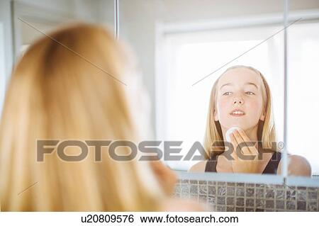 Stock Photograph - "Young girl in bathroom, looking in mirror, cleansing face". Fotosearch