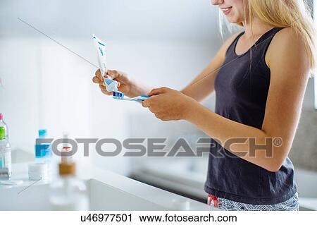 Stock Image - "Young girl in bathroom, squeezing toothpaste onto brush". Fotosearch
