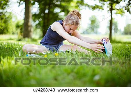 Stock Image - "Young girl in park, doing stretches on grass". Fotosearch