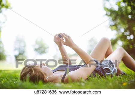 Stock Photograph - "Young girl in park, lying on grass, looking at mp3 player". Fotosearch