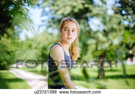 Stock Photo - "Young girl in park, wearing earphones, looking away". Fotosearch