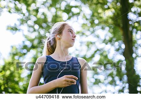 Stock Photo - "Young girl in park, wearing earphones, low angle view". Fotosearch