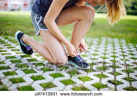 Stock Image - "Young girl, outdoors, crouching, tying shoe lace, low section". Fotosearch