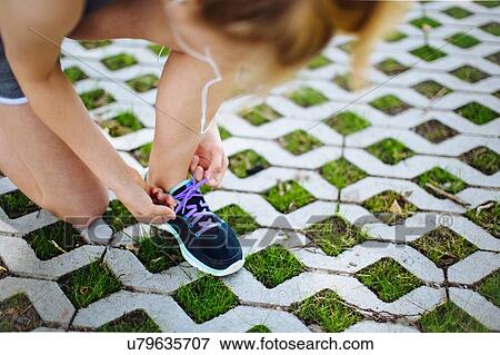 Stock Photo - "Young girl, outdoors, crouching, tying shoe lace, elevated view". Fotosearch
