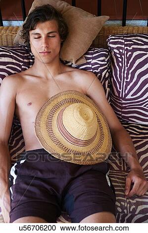 Stock Image - Young man lying on daybed with sunhat in stomach. Fotosearch