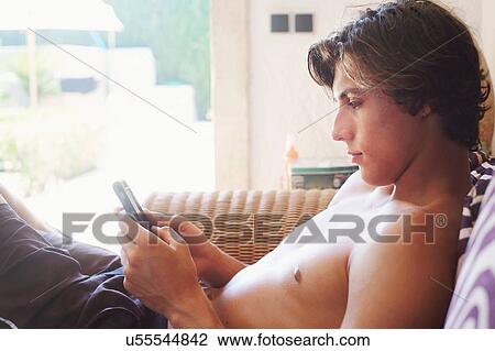 Stock Image - Young man reading smartphone texts on patio chair. Fotosearch