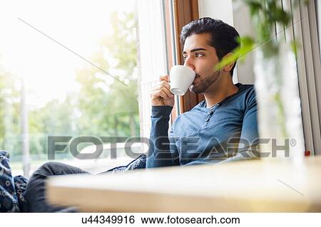 "Young man sitting in front of window drinking coffee, looking away" View Large Photo Image Stock Photograph - "Young man sitting in front of window drinking coffee, looking away". Fotosearch