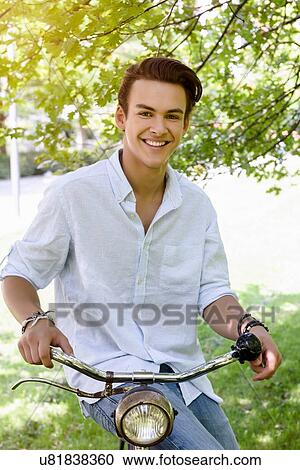 Young man sitting side saddle on bicycle looking at camera smiling View Large Photo Image Stock Image - Young man sitting side saddle on bicycle looking at camera smiling. Fotosearch