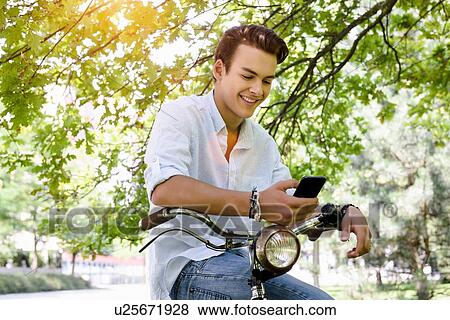 Young man sitting side saddle on bicycle looking smartphone smiling View Large Photo Image Stock Photo - Young man sitting side saddle on bicycle looking smartphone smiling. Fotosearch